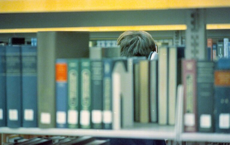 図書館の本棚で本を探す人（学習のイメージ写真）
