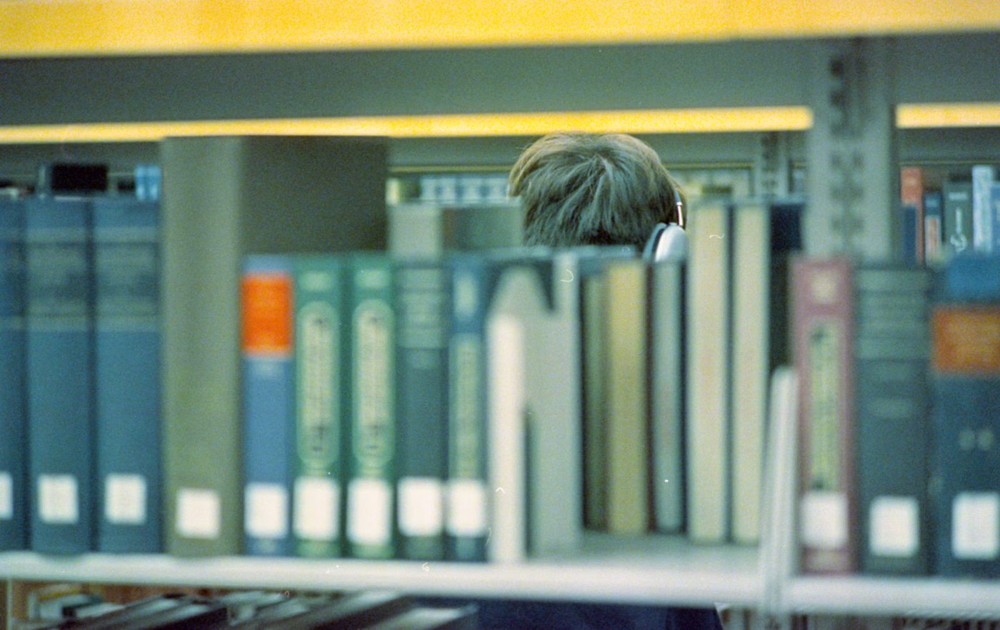 図書館の本棚で本を探す人（学習のイメージ写真）